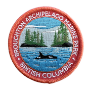 An embroidered circular patch for Broughton Archipelago Marine Park, British Columbia, featuring a blue water scene with a black and white orca, green pine trees, and a coral-red border with white text.