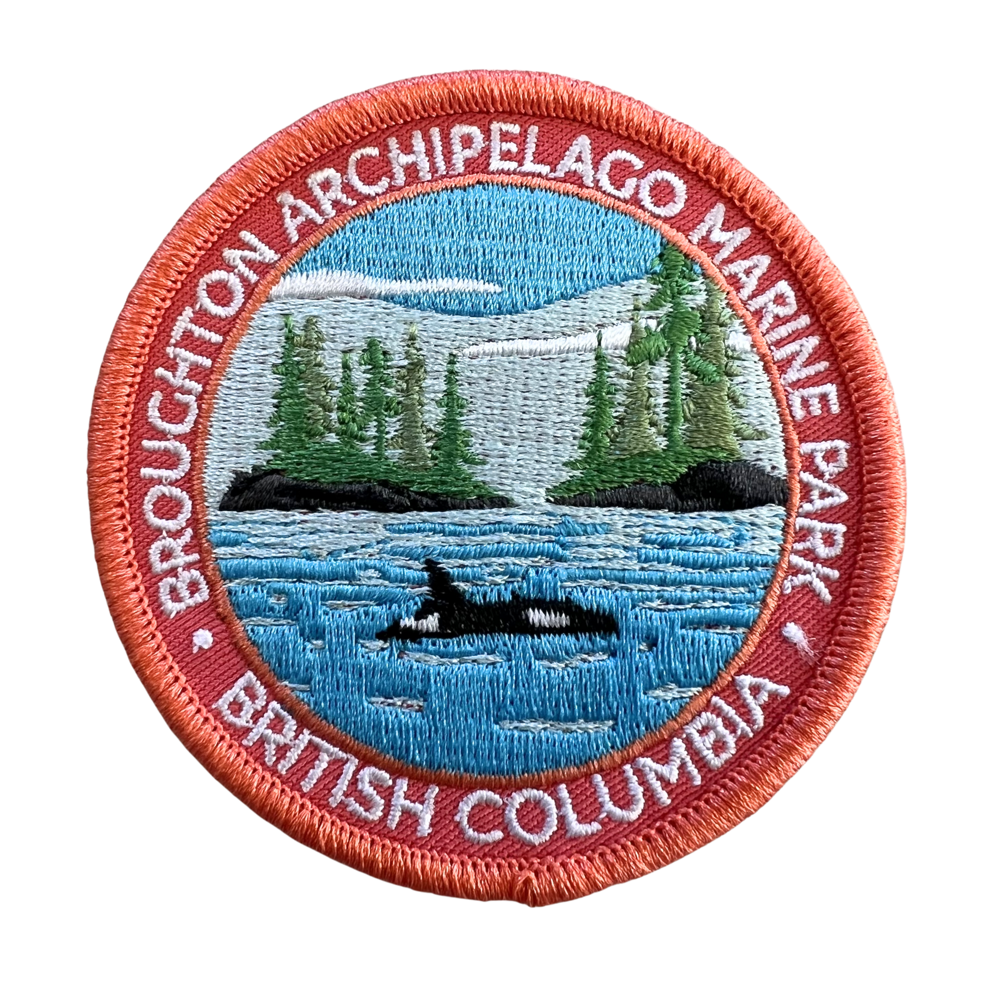 An embroidered circular patch for Broughton Archipelago Marine Park, British Columbia, featuring a blue water scene with a black and white orca, green pine trees, and a coral-red border with white text.