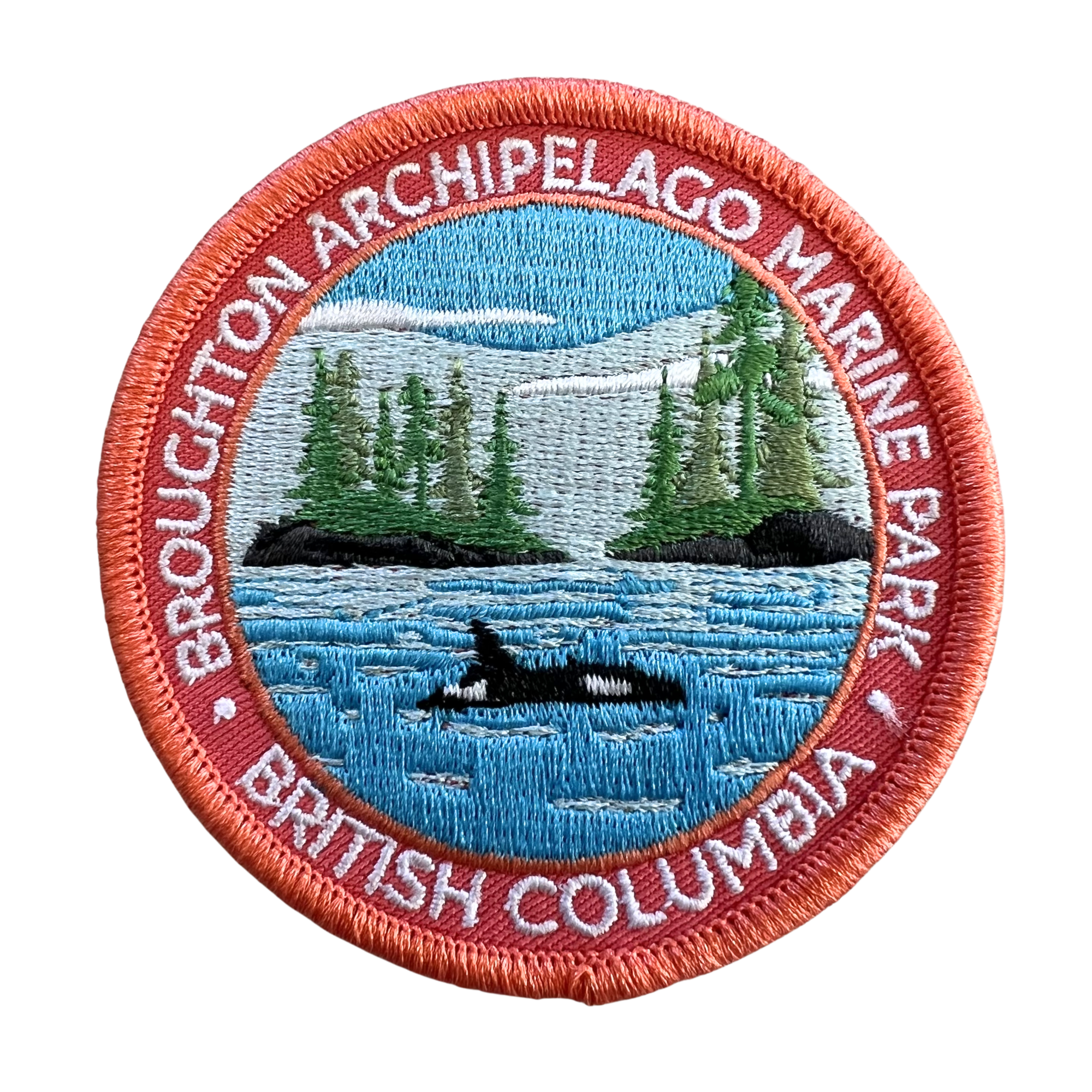 An embroidered circular patch for Broughton Archipelago Marine Park, British Columbia, featuring a blue water scene with a black and white orca, green pine trees, and a coral-red border with white text.
