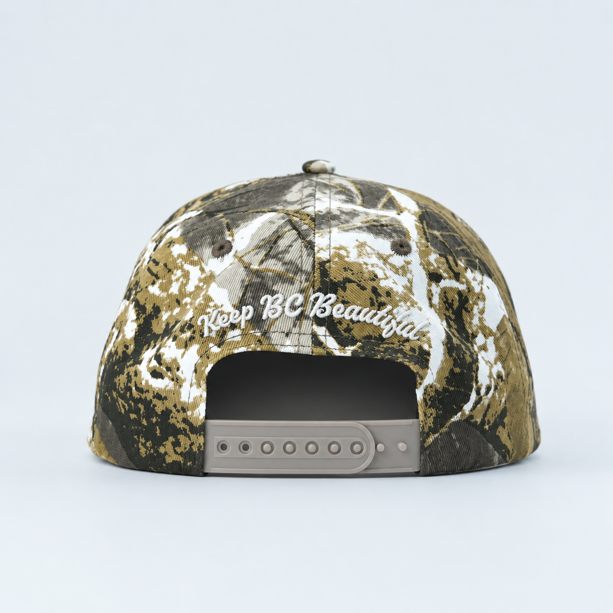A structured baseball cap fBack detail with "keep BC Beautiful" embroidered on on a realistic woodland camouflage pattern with brown, black, green, and white tones, shown from a side profile on a light gray background.