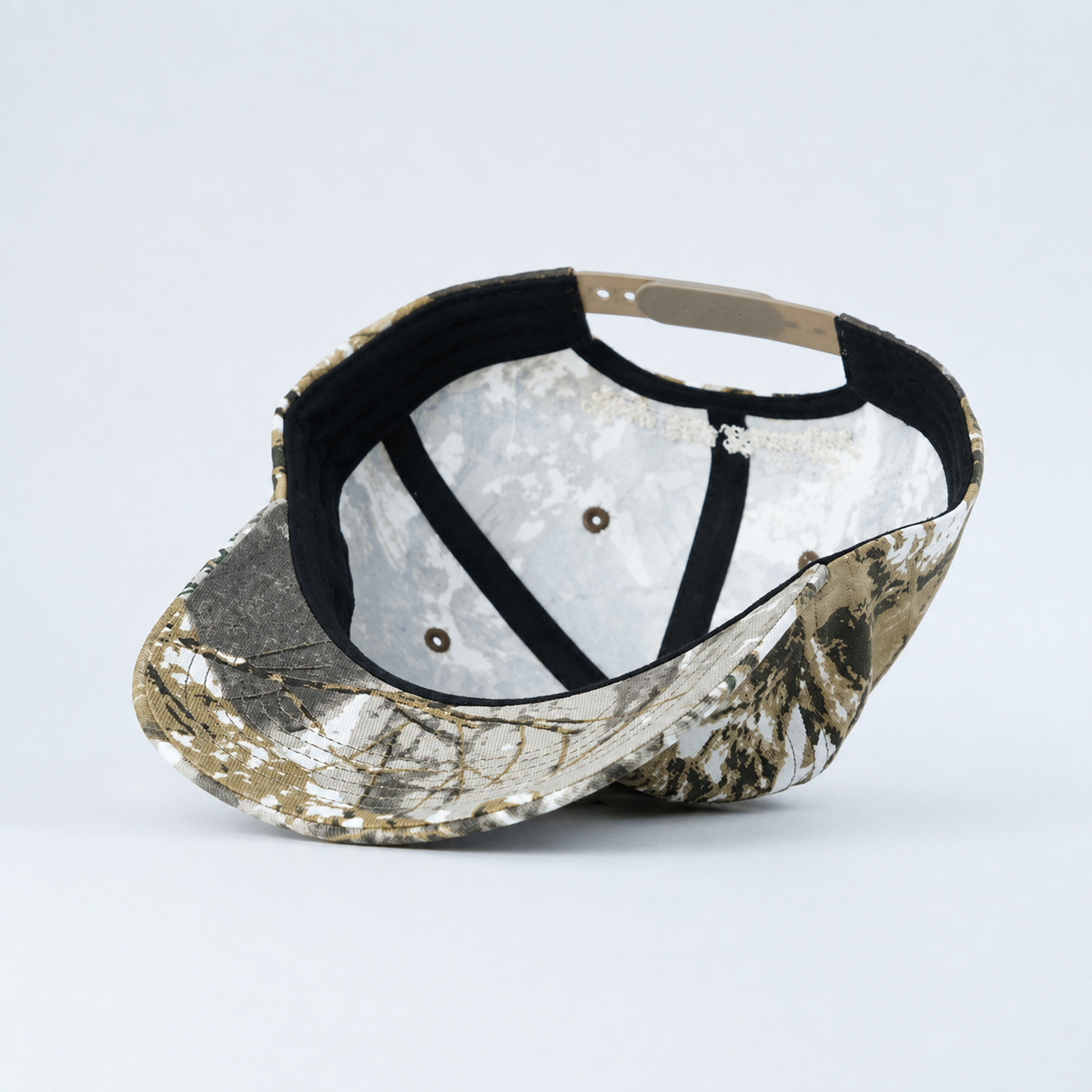 A baseball cap with a realistic woodland camouflage pattern on the exterior and a white textured fabric interior, shown from an overhead angle on a light gray background.