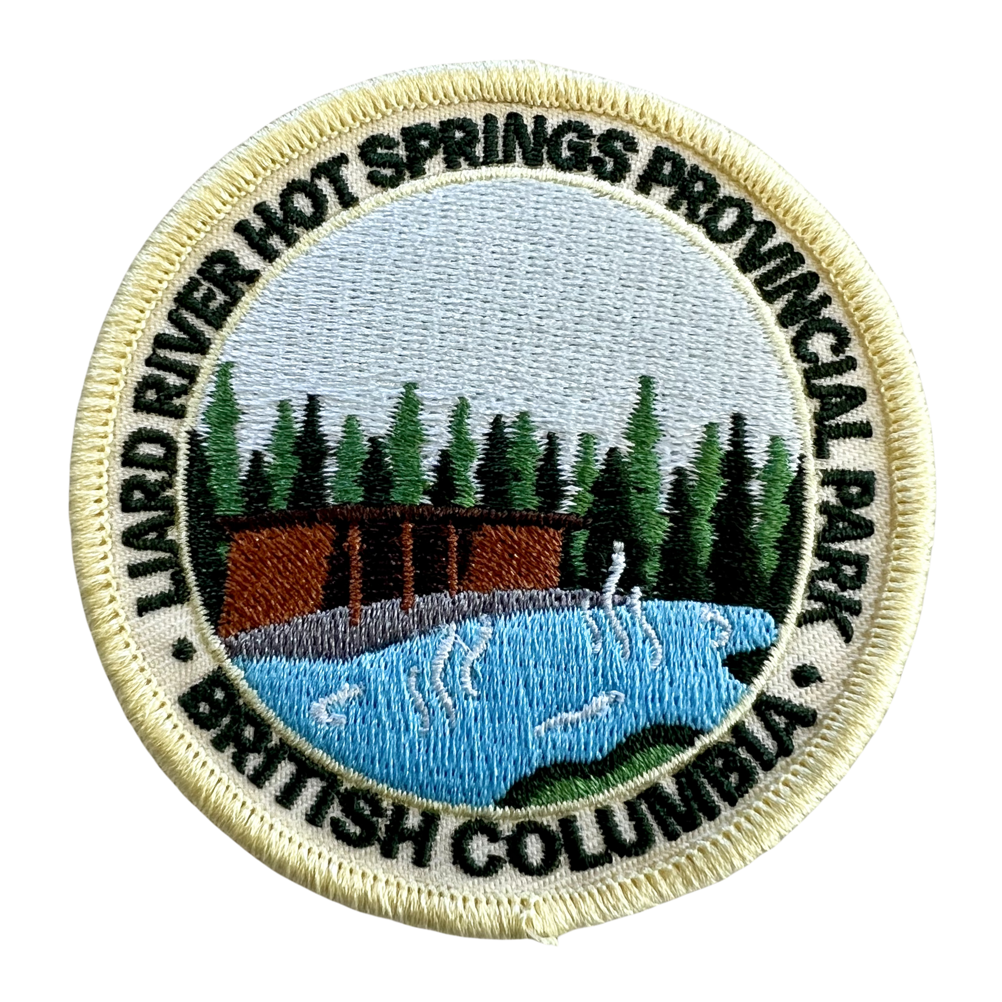 An embroidered circular patch for Liard River Hot Springs Provincial Park in British Columbia, featuring a scenic landscape with a cabin, pine trees, blue water, and black text on a cream background.