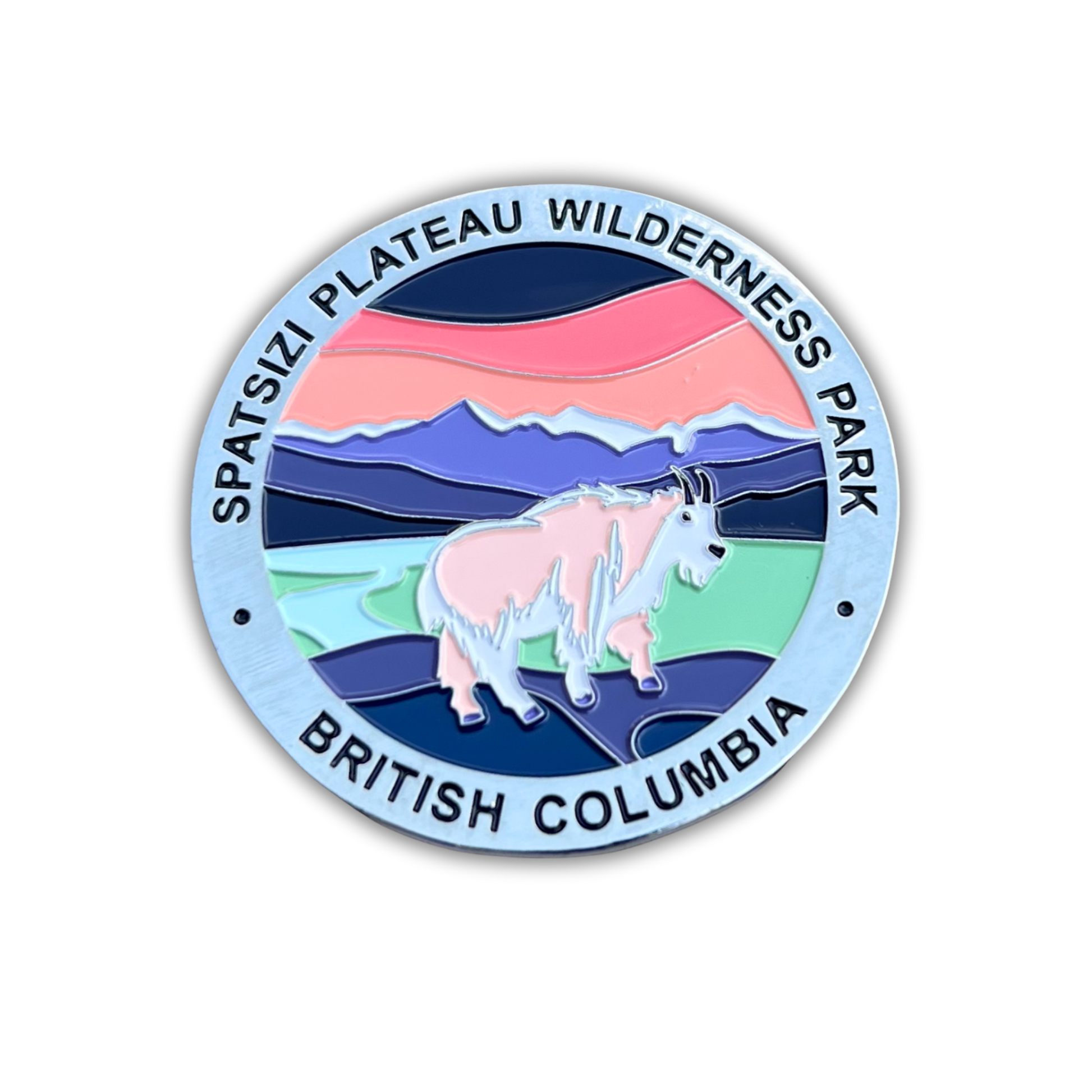A circular enamel-style park emblem magnet reading 'SPATSIZI PLATEAU WILDERNESS PARK' and 'BRITISH COLUMBIA,' featuring a mountain goat in front of layered blue, pink, green, and purple landscape bands on a white background.