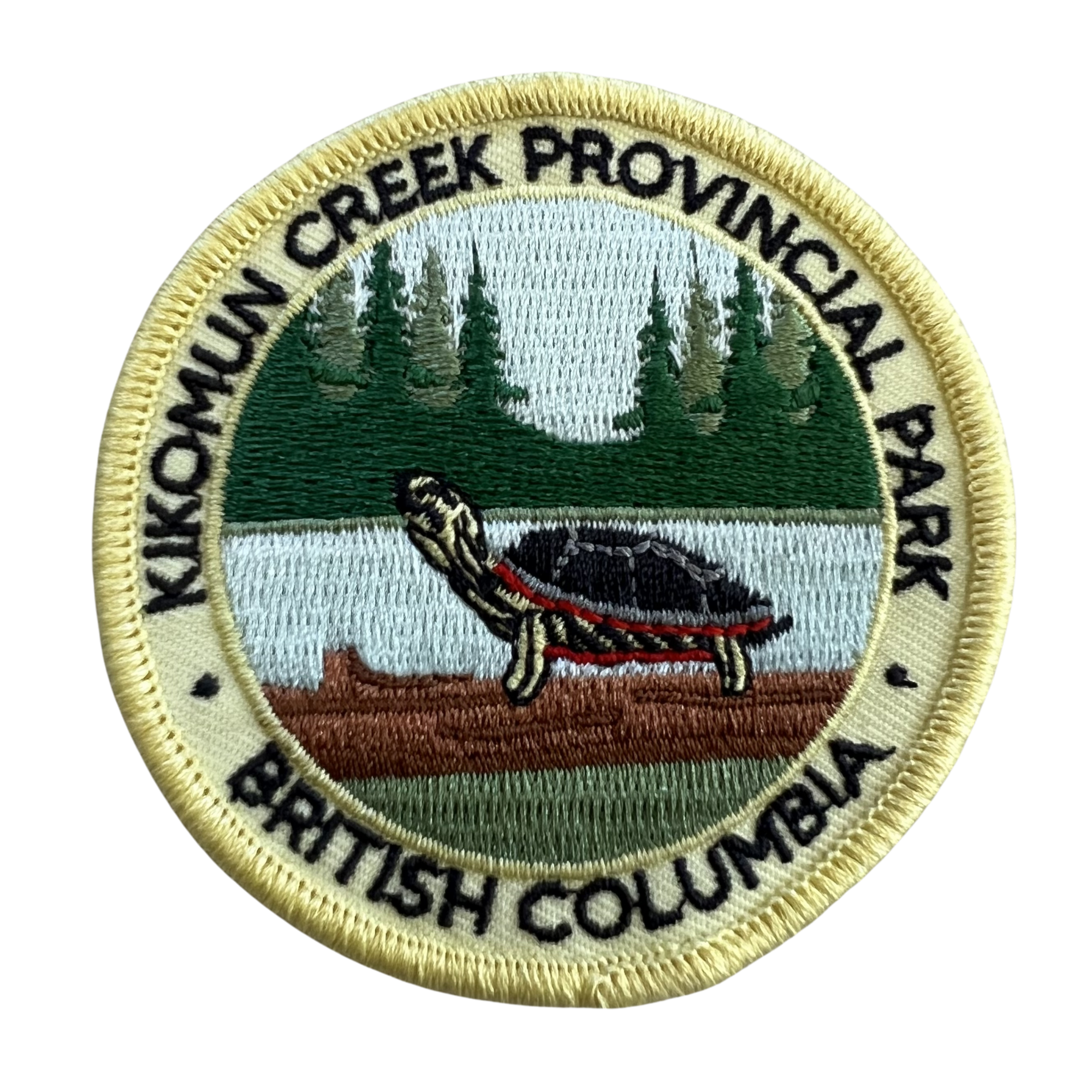 A circular embroidered patch for Kikomun Creek Provincial Park, British Columbia, featuring a painted turtle on a log by a lake with pine trees in the background, surrounded by black embroidered text on a cream border.