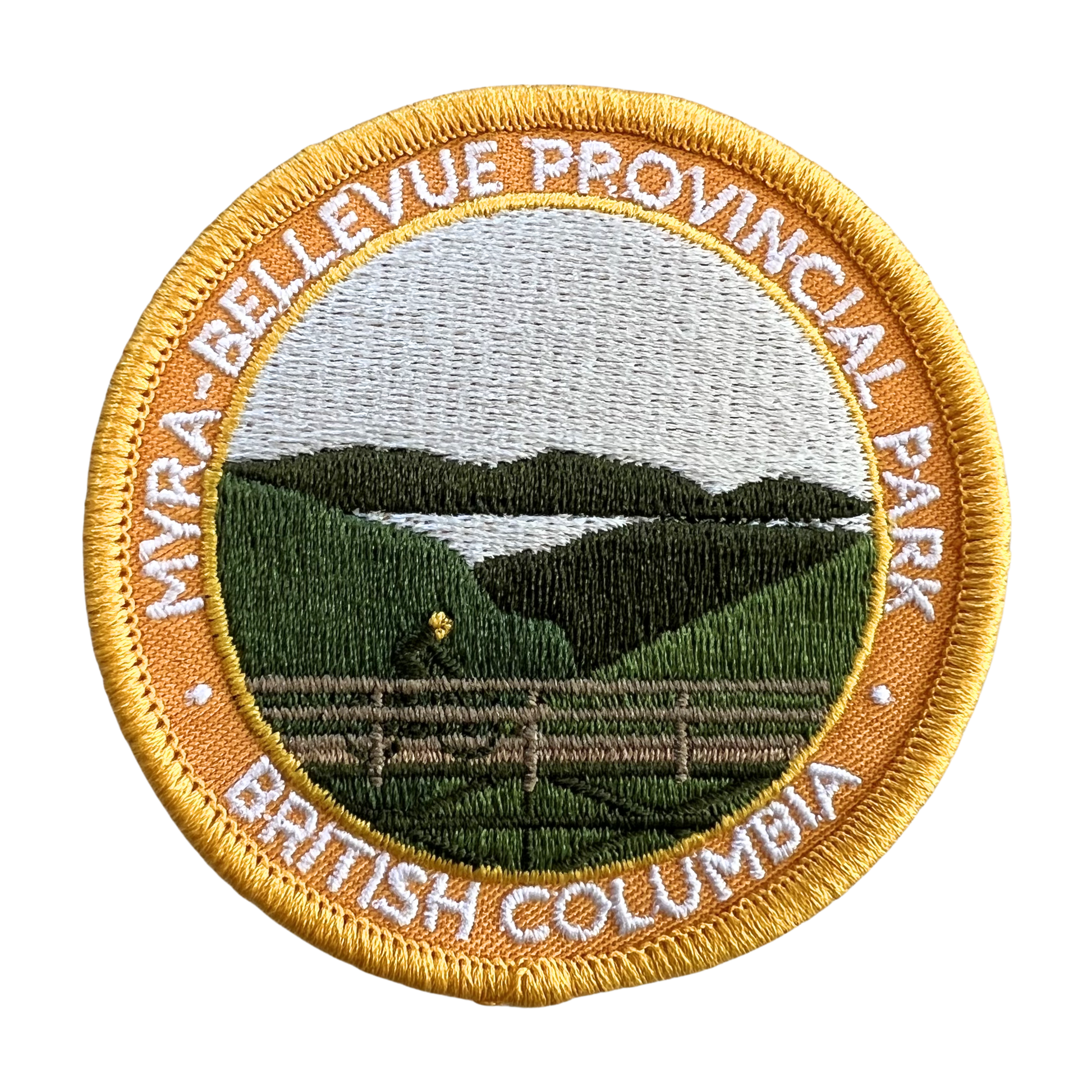 An embroidered circular patch for Myra-Bellevue Provincial Park, British Columbia, featuring a landscape design with green hills, a lake, and a fence, surrounded by a gold border with white text.