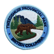 An embroidered circular patch for Tweedsmuir Provincial Park, British Columbia, featuring a brown grizzly bear, green pine trees, blue mountains, and a light blue border with dark blue text.